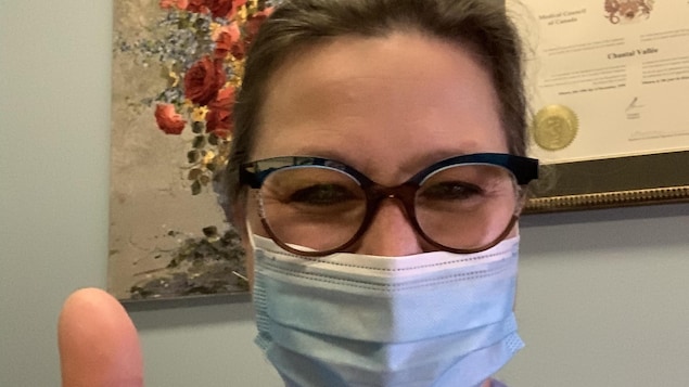 Photo selfie de la docteure en tenue d'hôpital, portant un masque chirurgical et faisant un pouce en l'air.