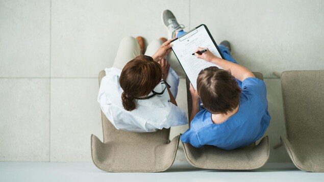 Vue aérienne de deux soignants assis sur des chaises qui remplissent ensemble un formulaire médical.