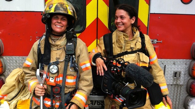 Deux femmes en tenue de pompière, l'une tient une caméra à la main.