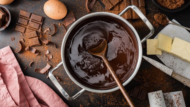 Du beurre, des œufs, du cacao en poudre, des tablettes de chocolat et une casserole de chocolat fondu sur une table.