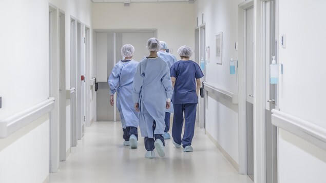 Quatre employés médicaux marchent de dos dans un couloir d'hôpital.