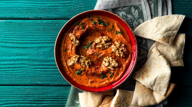 La tartinade est servie dans un bol, avec des noix sur le dessus, et des pains pitas. 