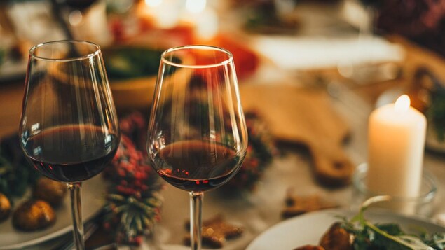 Deux verres de vin rouge posés sur une table de Fêtes avec des bougies.