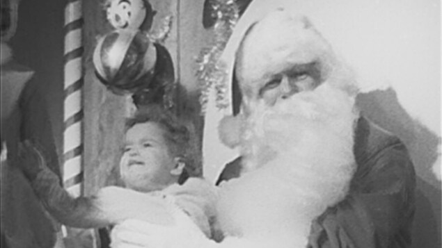 Image en noir et blanc du père Noël assis avec un enfant sur ses genoux. 