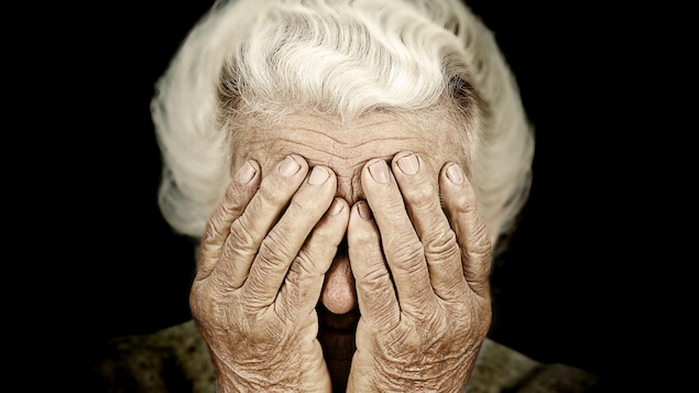 Une dame âgée se couvrant les yeux de ses mains. 