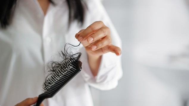 Une personne aux cheveux longs tient une brosse à cheveux.