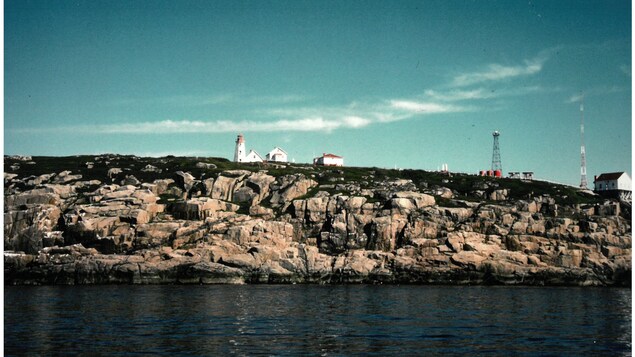 Le phare, d'autres bâtiments tout près et des antennes sur l’île rocheuse en 1985.