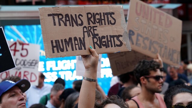 Une personne brandit une pancarte où il est écrit que « les droits des transgenres sont des droits de la personne ».