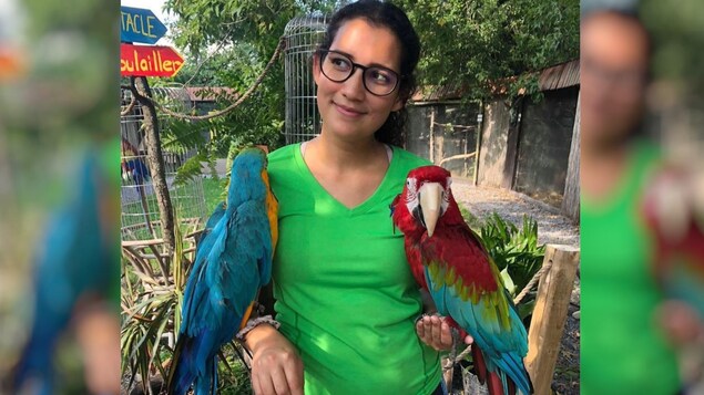 La femme tient deux perroquets sur ses bras.