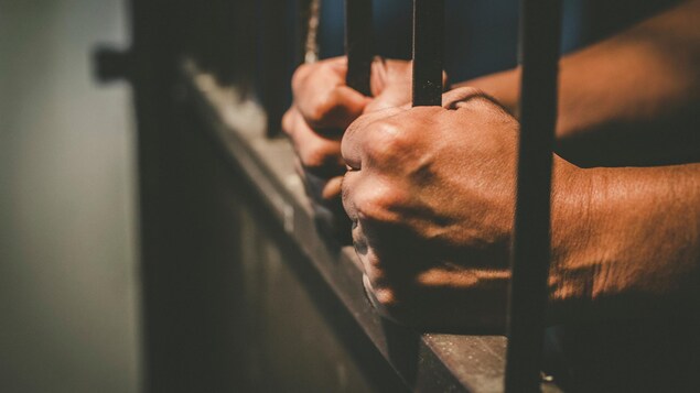 Deux mains tiennent des barreaux en prison.