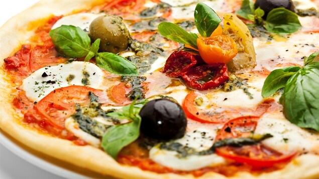 Une pizza garnie de tomates, de mozzarella, de pesto vert, d'olives et de basilic. 