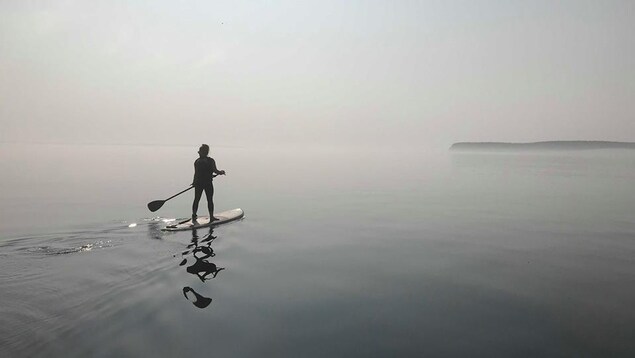 Une personne à planche à pagaie navigue dans la brume au large du Havre-Saint-Pierre.