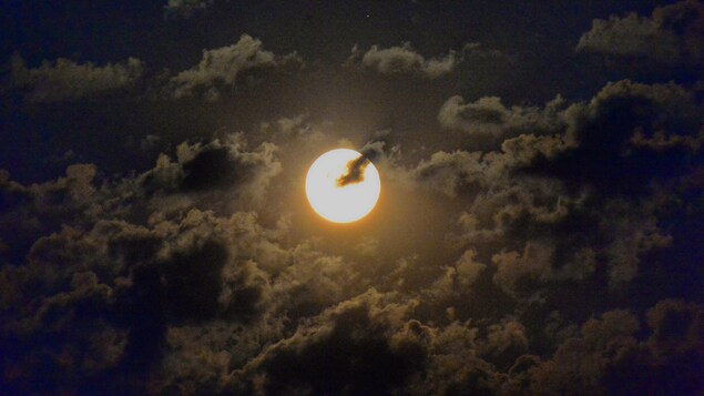 Une pleine lune dans un ciel ennuagé.