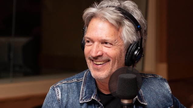 Claude Meunier, portant des écouteurs dans un studio radio, sourit.