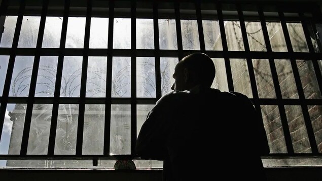 Un détenu regarde par une fenêtre avec des barreaux dans une prison.