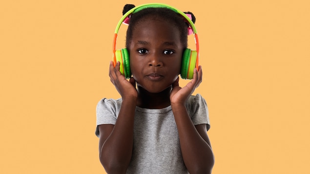 Une petite fille tient des écouteurs sur ses oreilles. 