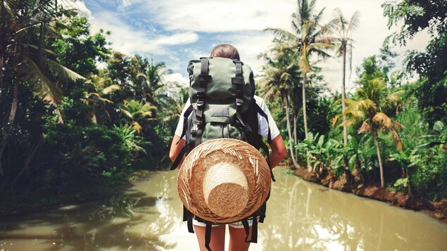 Une personne portant un sac à dos se tient devant une rivière.