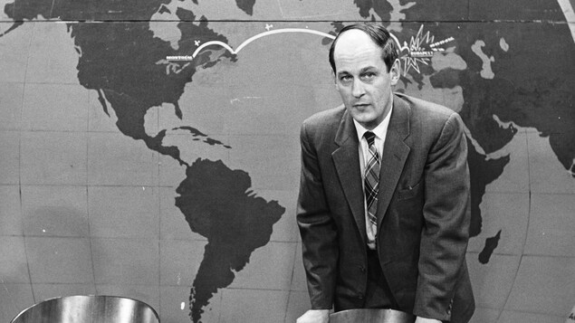 Debout devant une carte du monde, l'animateur René Lévesque est appuyé au dossier d'une chaise, une cigarette entre les doigts. Debout devant une carte du monde, l'animateur René Lévesque est appuyé au dossier d'une chaise, une cigarette entre les doigts.