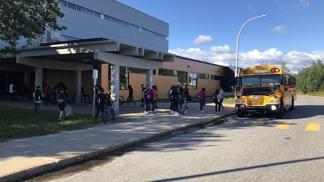 Des élèves et un autobus scolaire devant la polyvalente. 