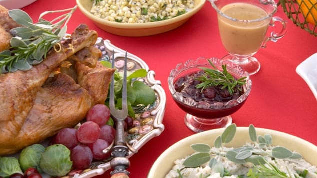Sur une table avec une nappe rouge de Noël, on voit une dinde rôtie, une sauce aux canneberges et une salade de poulet. 