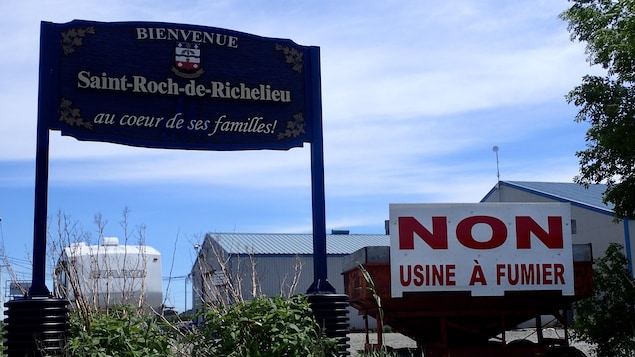 Une pancarte disant « Bienvenue à Saint-Roch-de-Richelieu » et, juste à côté, une pancarte disant « Non usine à fumier ».