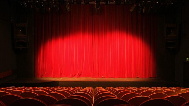 Une salle de spectacle vide avec un éclairage sur la scène, avec de gros rideaux.