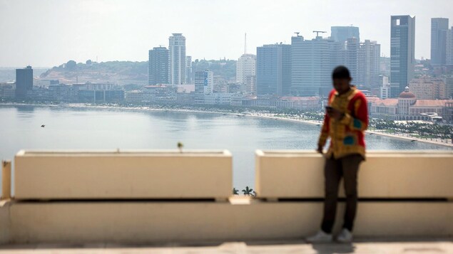 Un homme regarde son téléphone alors que se profile derrière lui Luanda, en Angola.