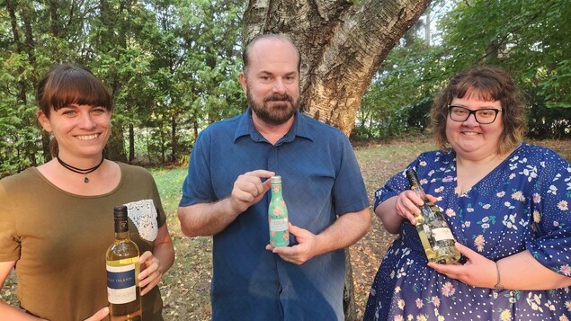 Trois personnes devant un arbre, tenant dans leurs mains chacun une bouteille de vin.