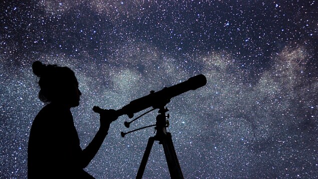 Une jeune fille regarde les étoiles avec un télescope.