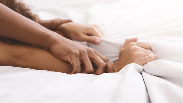 Les bras d'un couple s'entrecroisent sur les draps d'un lit. 