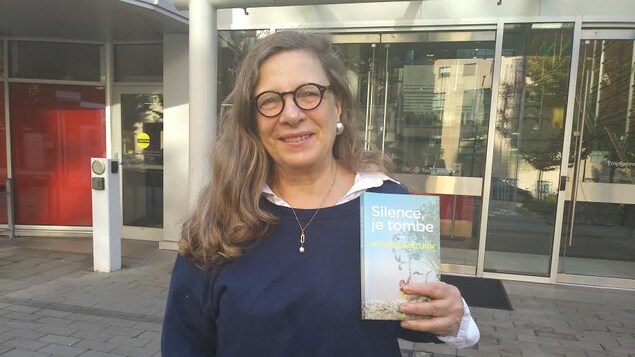 Une femme se tient debout avec son livre qu'elle tient dans sa main.
Elle est à l'extérieur, devant la porte d'entrée de Radio-Canada.