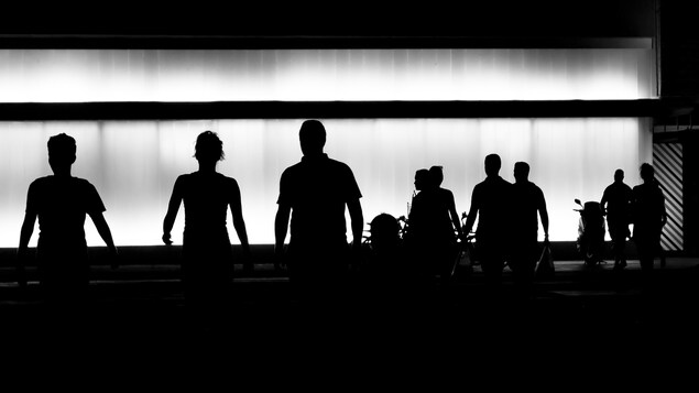 Image en noir et blanc montrant des silhouettes de personnes marchant dans une rue.