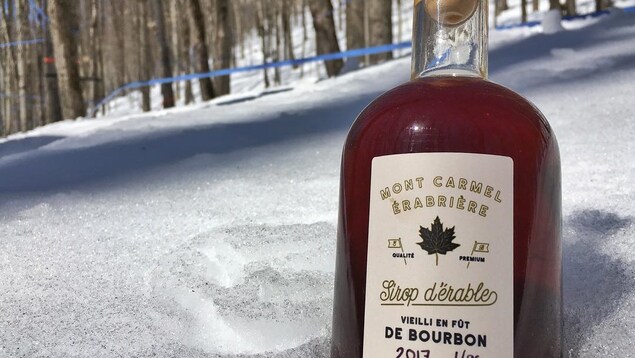 Une bouteille en verre de sirop d'érable posée sur de la neige. Une bouteille en verre de sirop d'érable posée sur de la neige.