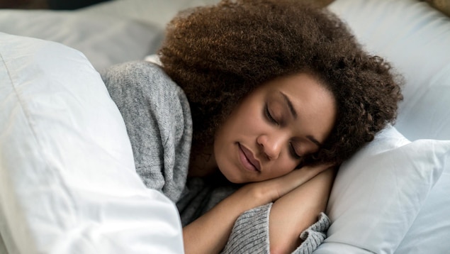 Une femme noire dort dans un lit de draps blancs.