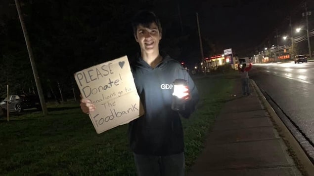 Un jeune homme sur le trottoir avec un panneau à la main.