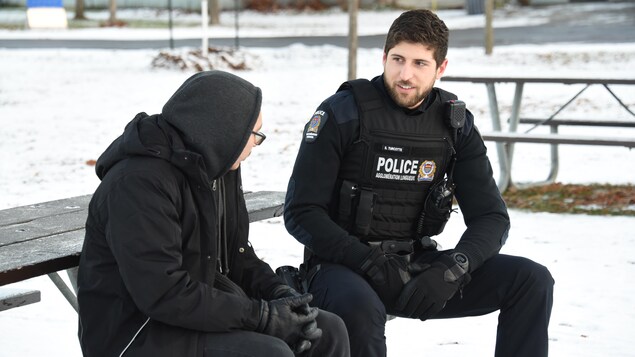 Un policier discute avec un homme assis à une table à pique-nique un jour d'hiver. 