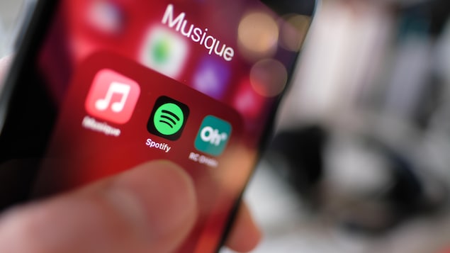 Le logo de l'application Spotify sur un téléphone qui s'apprête à être ouverte par un doigt.