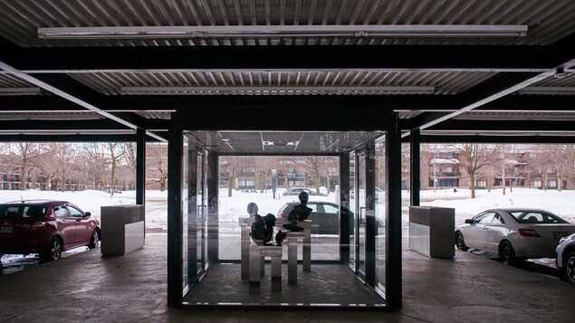 Une exposition de statues de têtes sous une grande boîte de verre, au cœur d'une ancienne station=service.