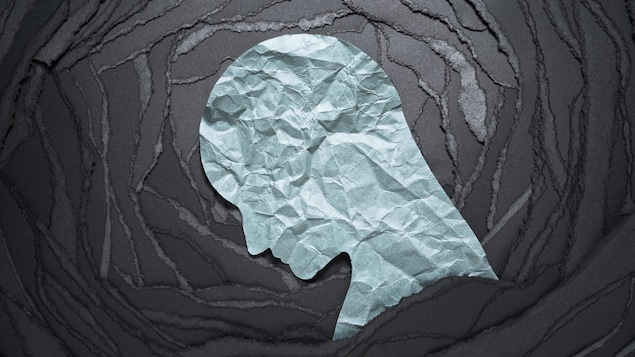 Image conceptuelle d'une émotion négative : un silhouette de tête en papier blanc froissé sur fond de papier noir déchiré.