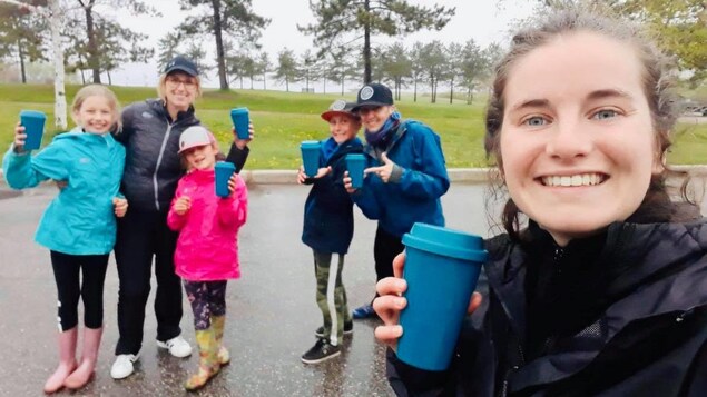Des personnes souriantes, tenant des tasses réutilisables, dans un stationnement, dehors.