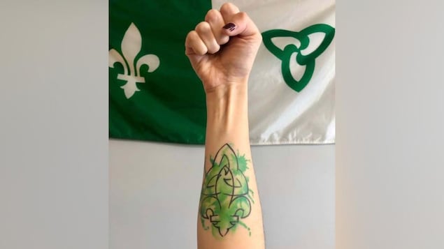 Tatouage d'un drapeau franco-ontarien sur l'avant bras, devant un drapeau franco-ontarien.