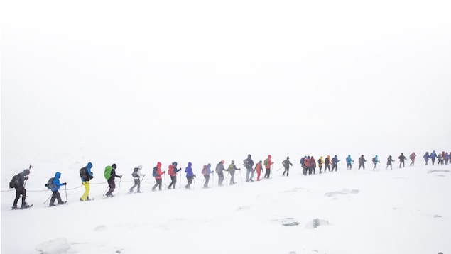 Une trentaine de personnes en raquett se suivent en file dans une tempête de neige.