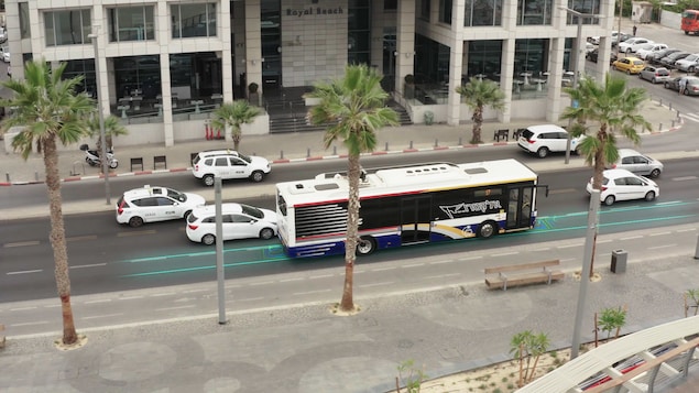 Un autobus roule sur une route, sur laquelle on voit des lignes bleues qui indiquent la position des conduites qui permettent aux véhicules de se recharger.