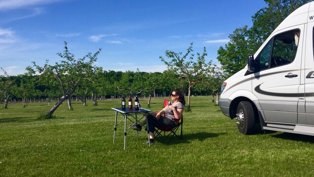 Une touriste pose près d'un verger, en buvant du vin près de son véhicule récréatif