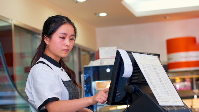 Une adolescente d'origine asiatique travaille dans une épicerie.