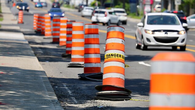 Des cônes orange dans la voie de droite d'une route endommagée lors de travaux routiers, un jour d'été. 
