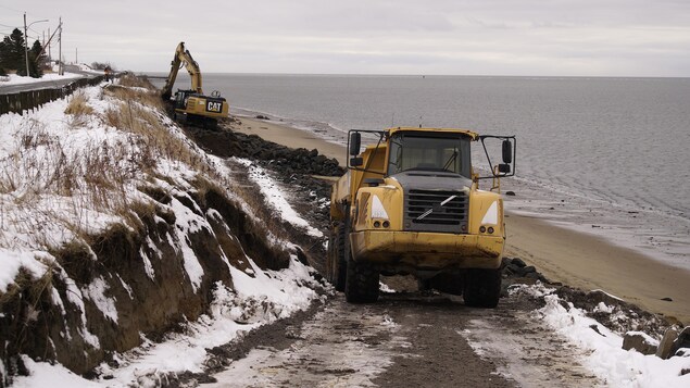 Un camion et une excavatrice sur une plage, en hiver.                