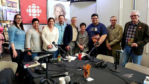 Quatre femmes et quatre hommes avec l'animateur de radio Éric Robitaille dans un Salon du livre à Hearst.