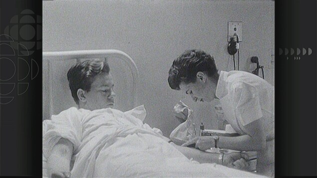 Image en noir et blanc montrant un jeune homme couché dans un lit d'hôpital et une infirmière lui faisant une prise de sang