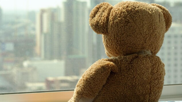 Un ourson en peluche triste regarde à l'extérieur.